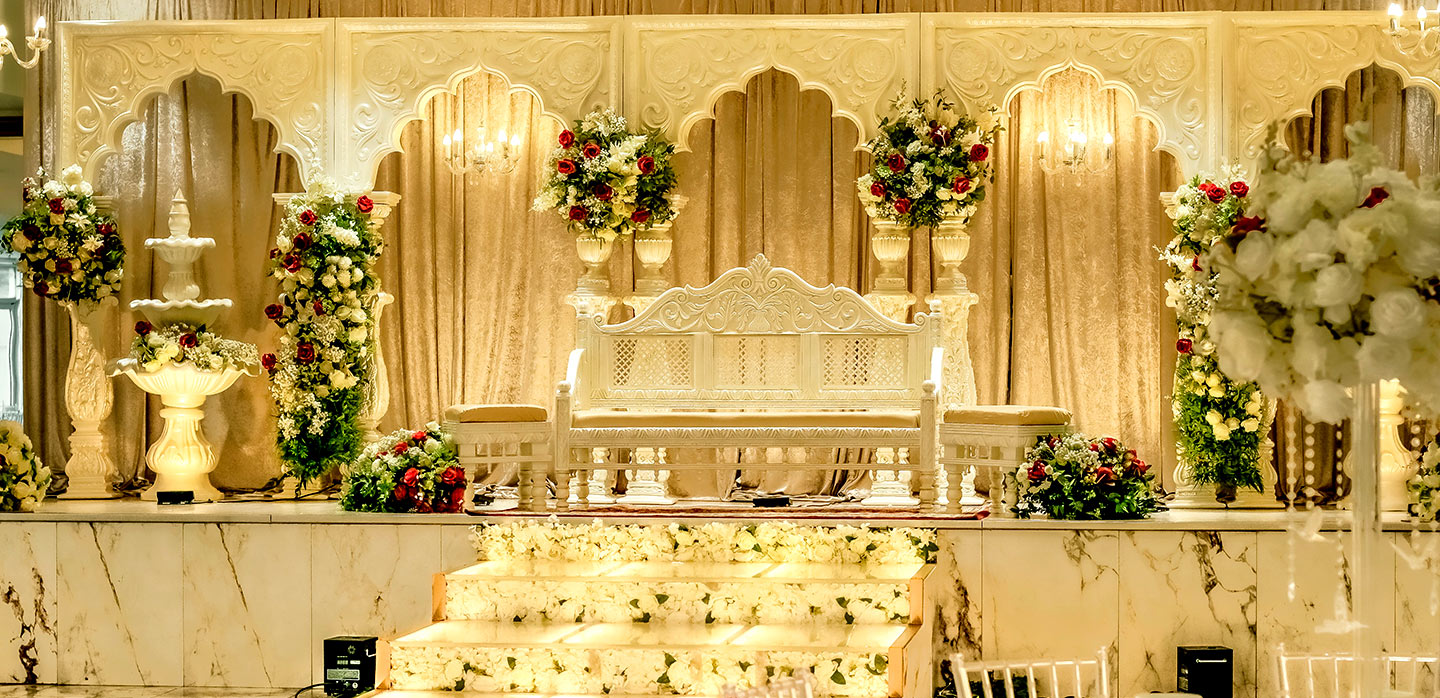 A lavish Greater Manchester wedding stage featuring an ornate white and gold backdrop, a decorative white bench, grand floral arrangements, and floral-covered steps, all beautifully illuminated by warm lighting.